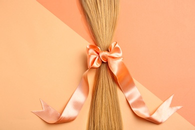 Photo of Blond hair tied with ribbon on color background, top view