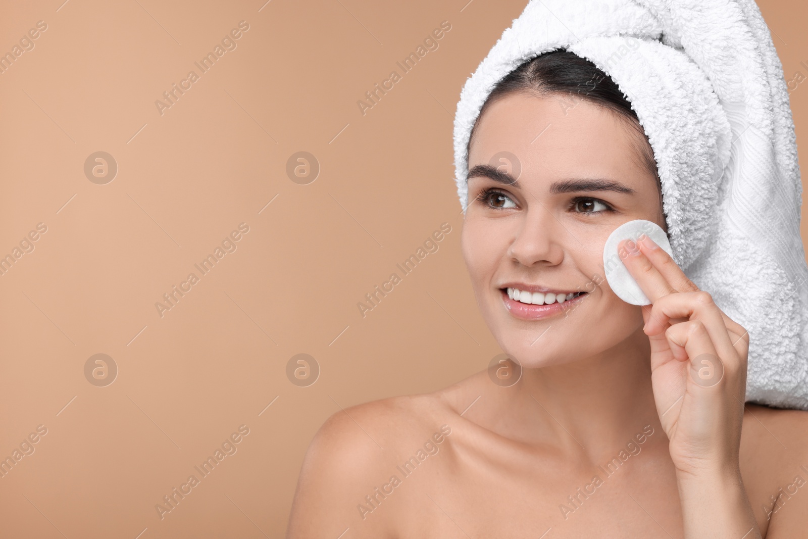 Photo of Young woman cleaning her face with cotton pad on beige background. Space for text