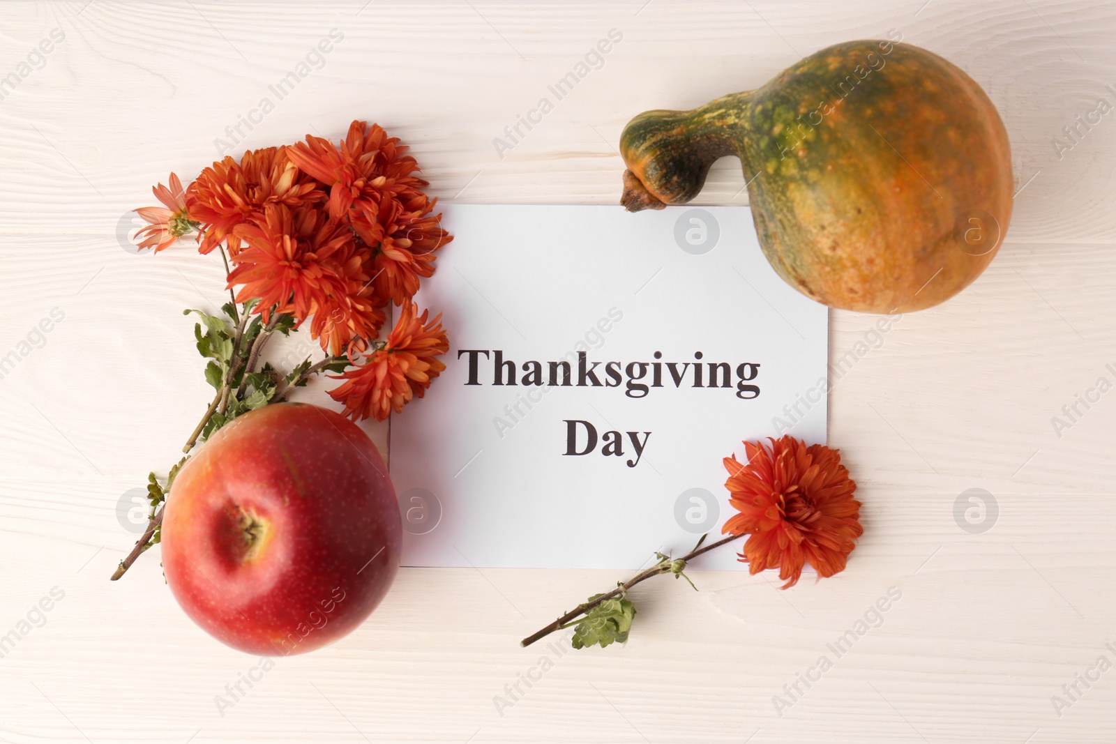 Photo of Thanksgiving day, holiday celebrated every fourth Thursday in November. Card, apple, pumpkin and chrysanthemum flowers on white wooden table, flat lay