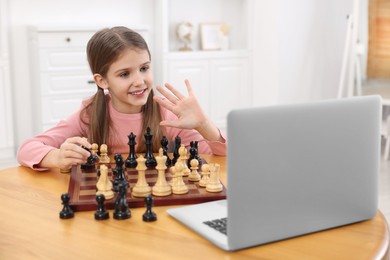 Photo of Cute girl learning to play chess with online tutor at home