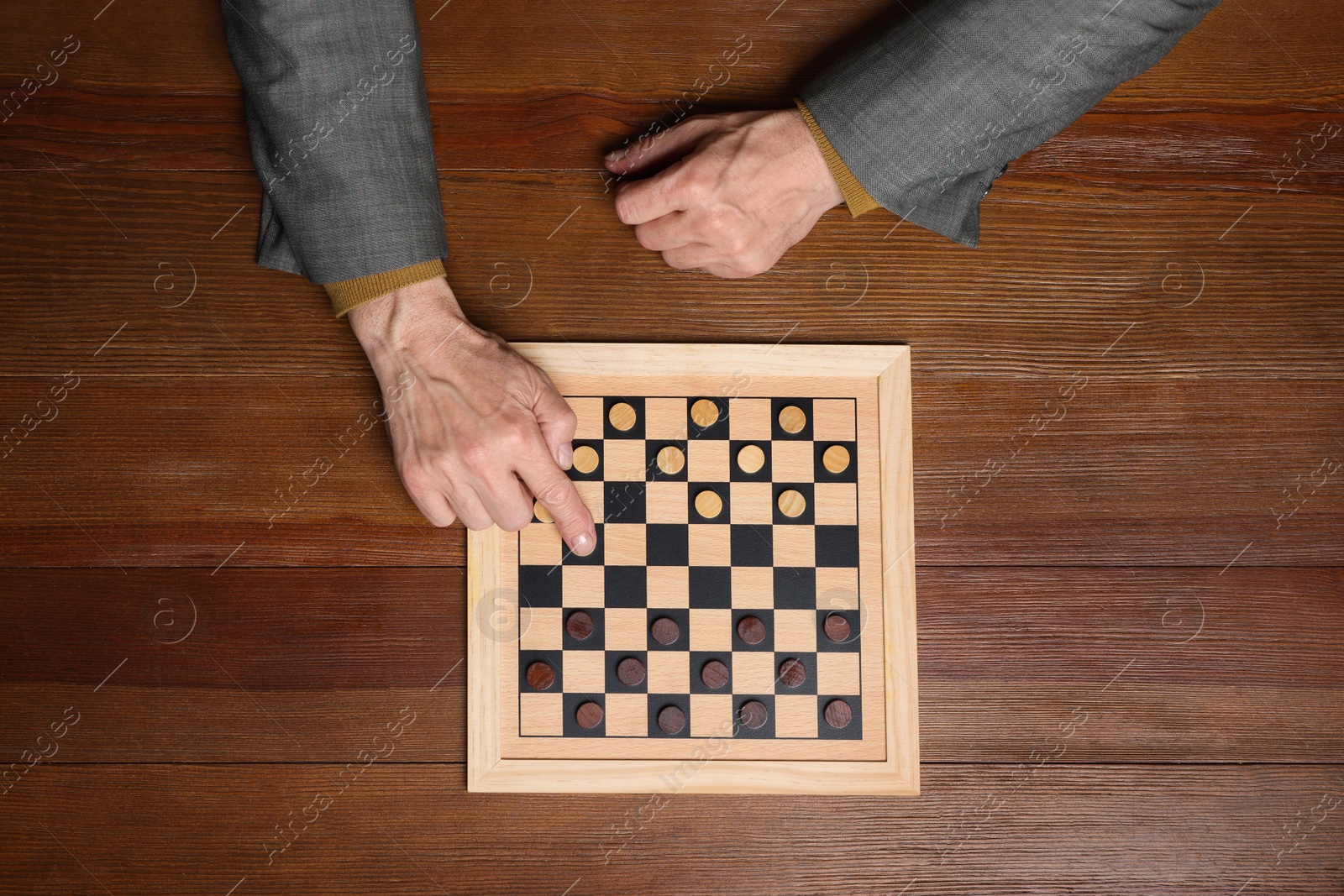 Photo of Playing checkers. Senior man thinking about next move at wooden table, top view