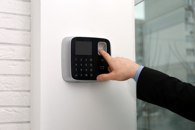 Photo of Man scanning fingerprint on alarm system indoors, closeup