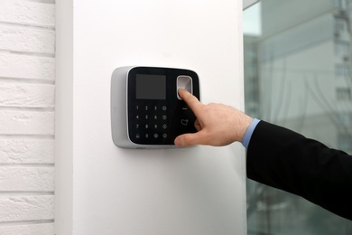 Man scanning fingerprint on alarm system indoors, closeup