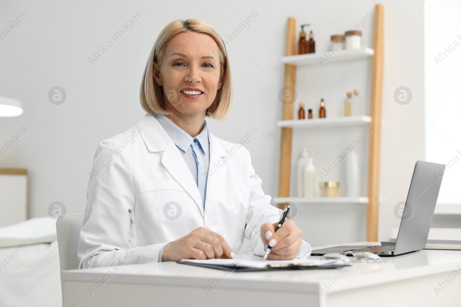 Photo of Portrait of happy dermatologist with pen at white table in clinic