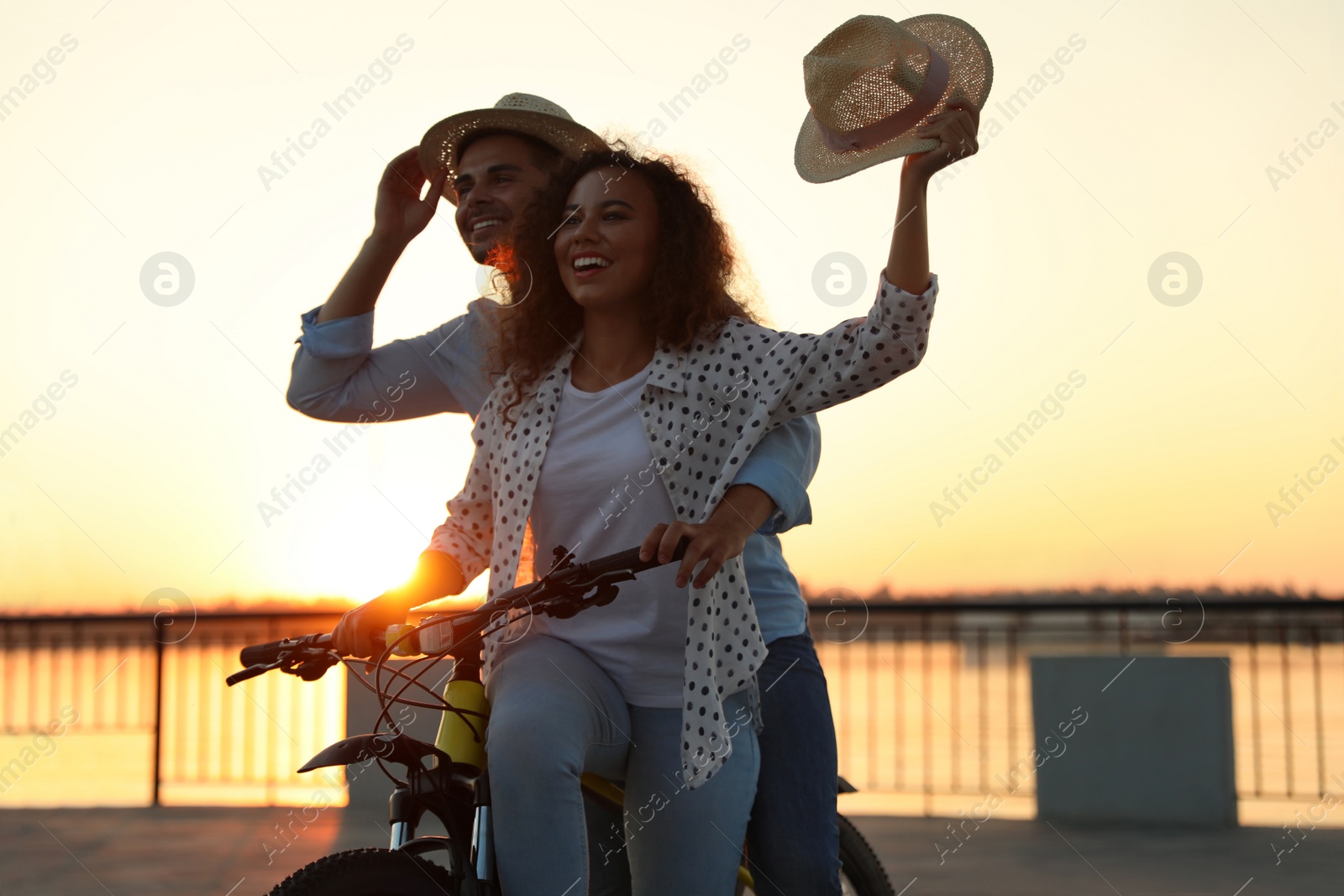 Photo of Young couple riding bicycle on city waterfront at sunset