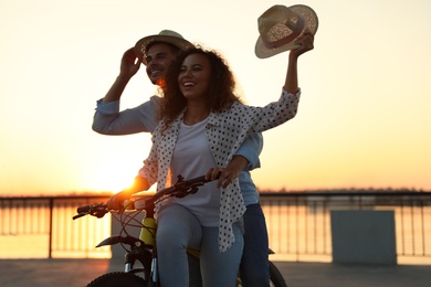 Photo of Young couple riding bicycle on city waterfront at sunset