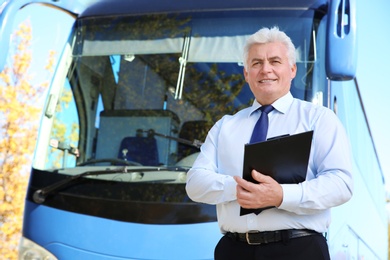 Professional driver with clipboard near bus. Passenger transportation