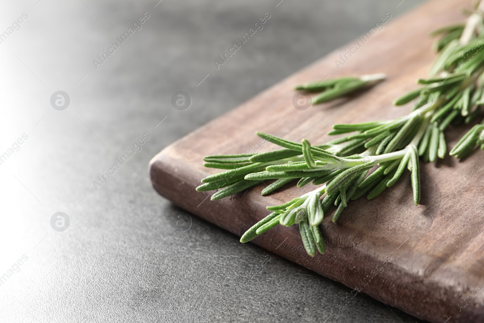 Photo of Wooden board with fresh rosemary twigs on table, closeup