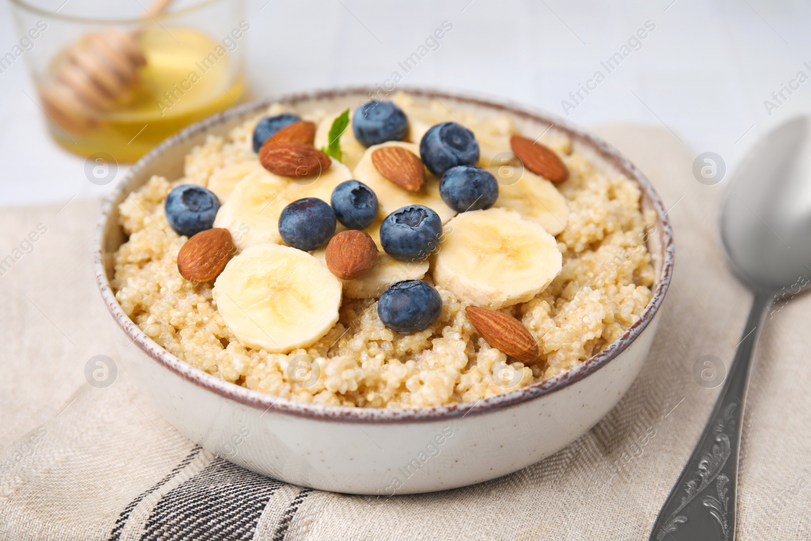 Photo of Bowl of delicious cooked quinoa with almonds, bananas and blueberries on kitchen towel, closeup