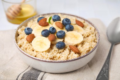 Photo of Bowl of delicious cooked quinoa with almonds, bananas and blueberries on kitchen towel, closeup