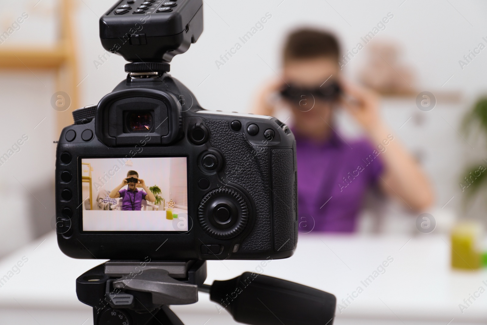 Photo of Cute little blogger with binoculars recording video at home, focus on camera