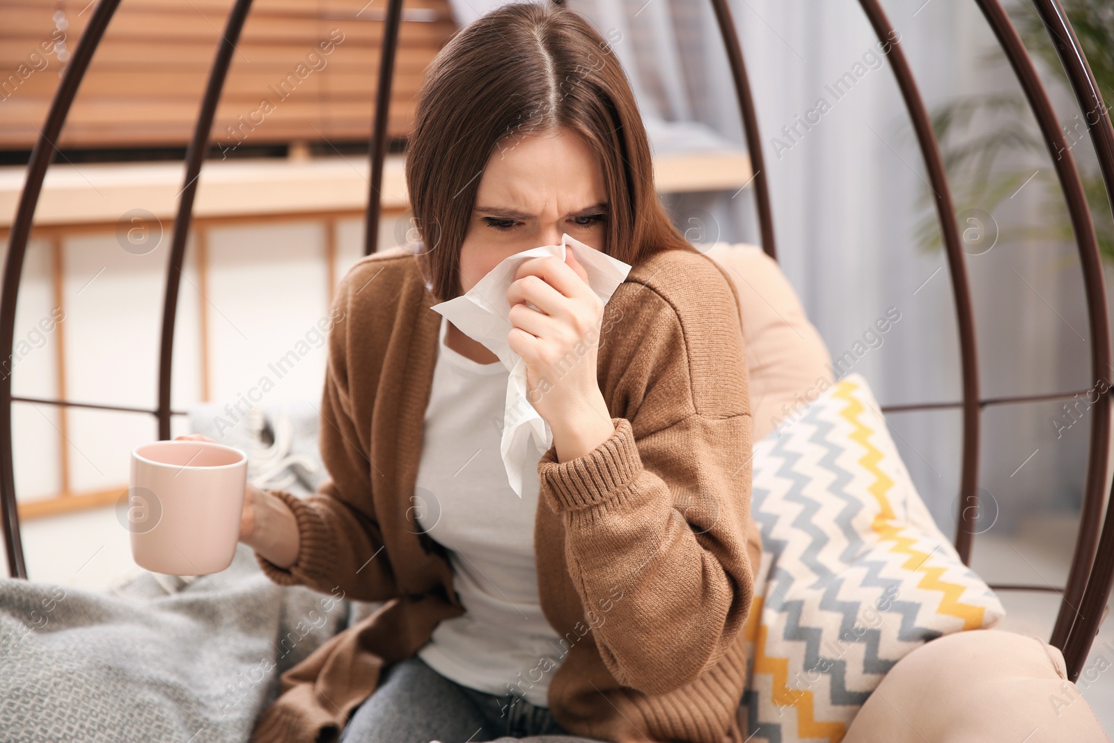 Photo of Sick young woman with cup of hot drink sneezing at home. Influenza virus