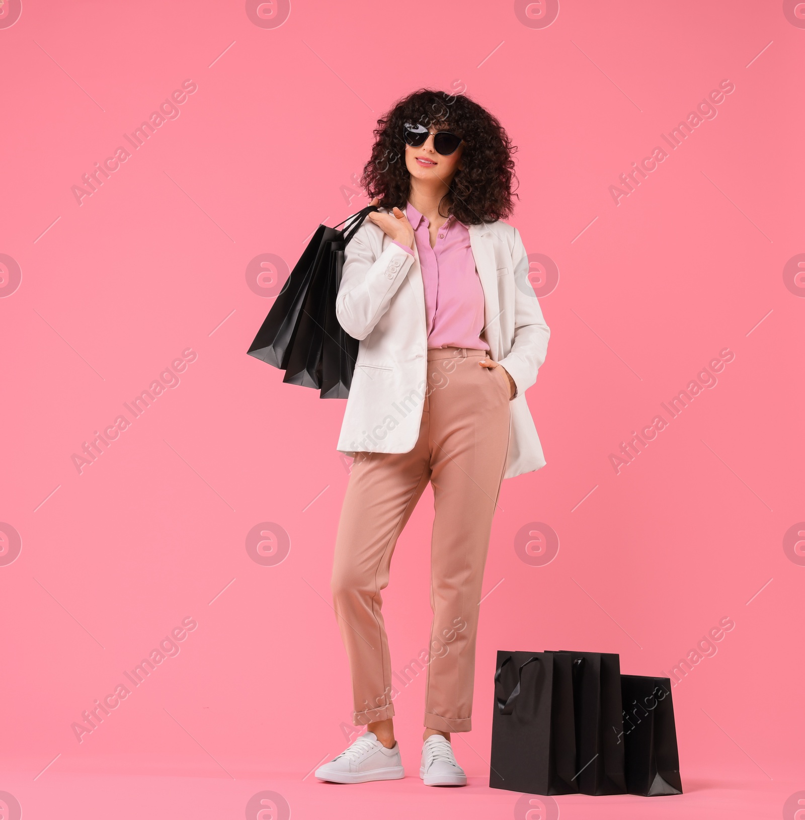 Photo of Happy young woman with shopping bags and stylish sunglasses on pink background. Space for text