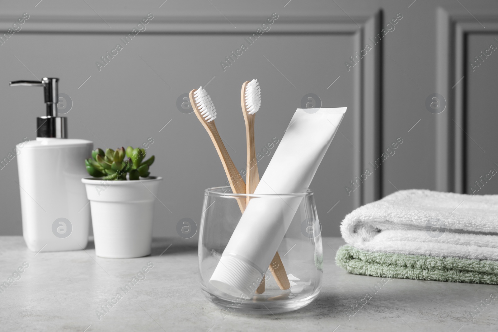 Photo of Bamboo toothbrushes in holder, toothpaste, houseplant and towels on light grey table