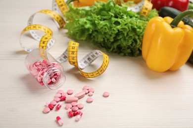 Photo of Weight loss pills, different vegetables and measuring tape on white wooden table