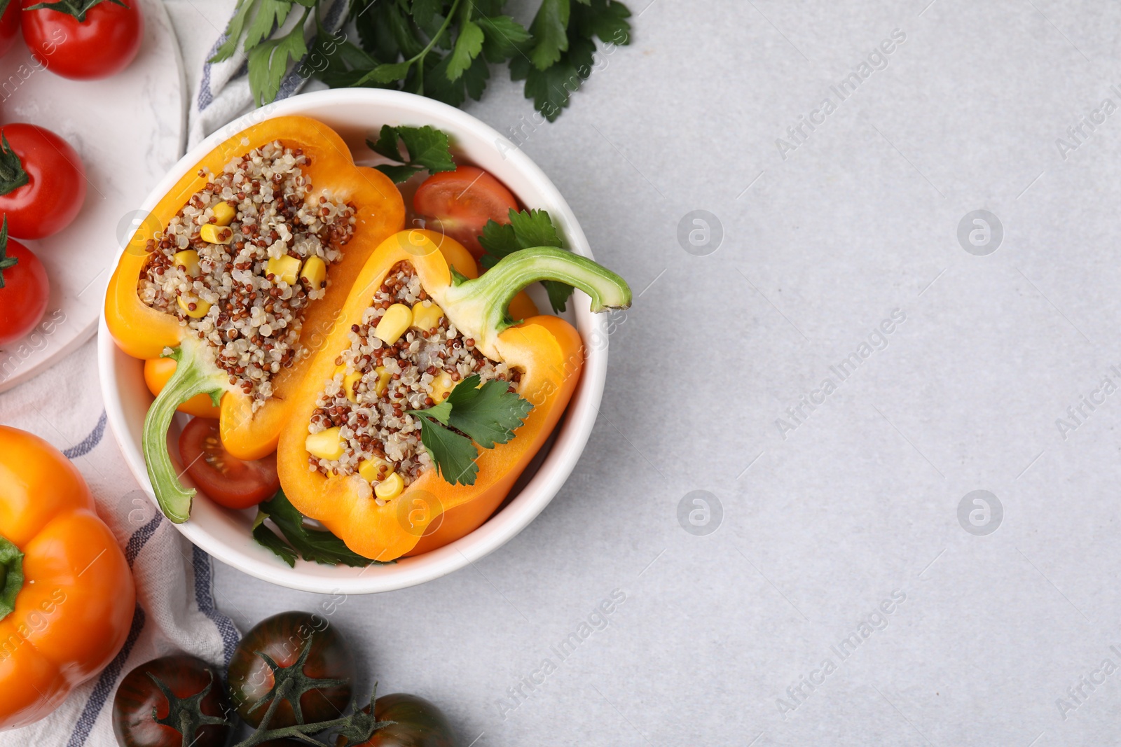 Photo of Quinoa stuffed bell pepper, tomatoes and parsley in bowl on light table, flat lay. Space for text