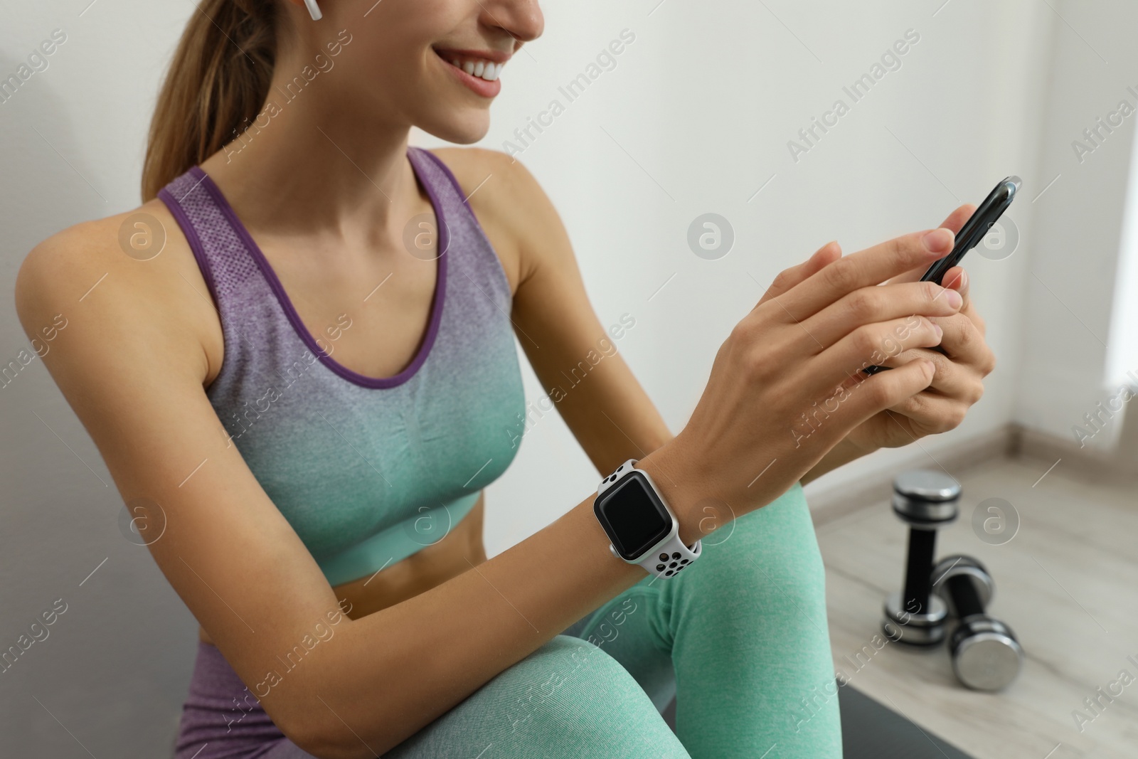 Photo of Young woman with modern smart watch and phone indoors, closeup
