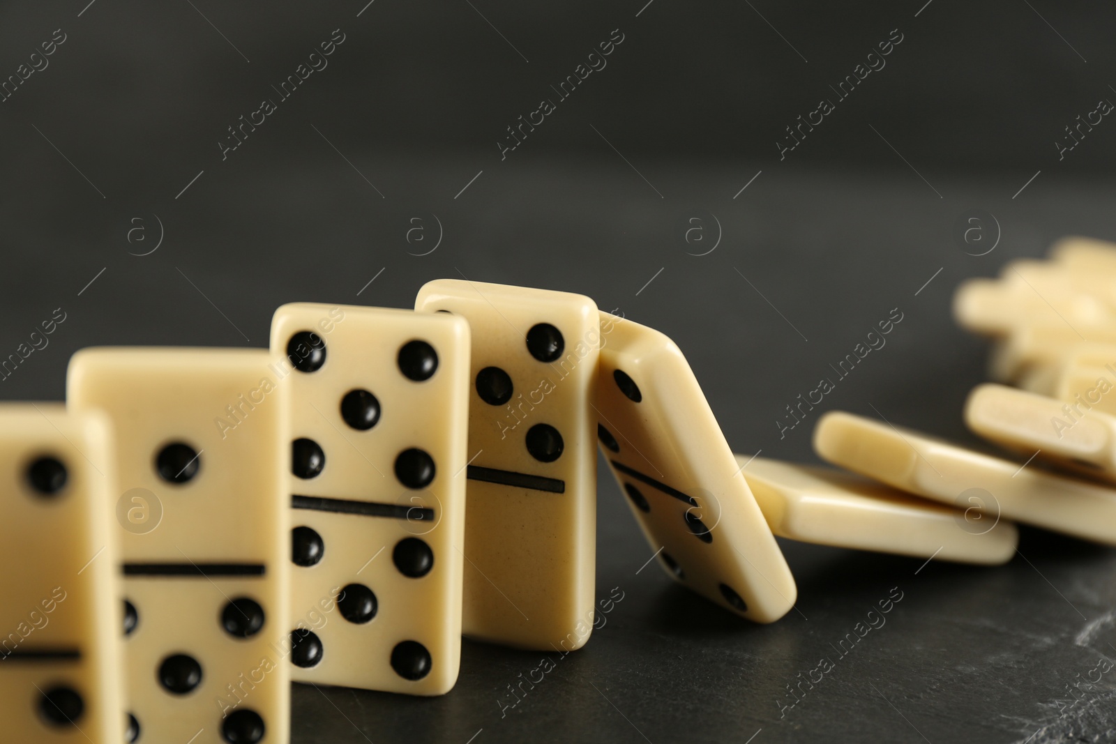 Photo of White domino tiles falling on dark grey table
