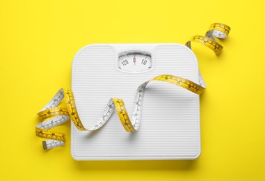 Scales and measuring tape on yellow background, top view