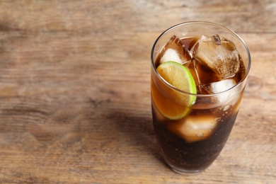 Photo of Glass of refreshing soda drink with ice cubes and lime on wooden table. Space for text