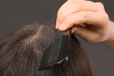 Photo of Woman with comb and dandruff in her dark hair on grey background, closeup