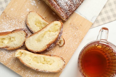 Pieces of delicious yeast dough cake and tea on white table, flat lay