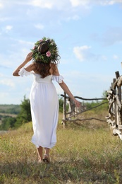 Photo of Young woman wearing wreath made of beautiful flowers outdoors on sunny day, back view