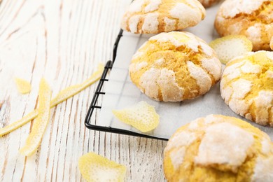 Photo of Cooling rack with delicious lemon cookies and citrus peels on white wooden table , closeup