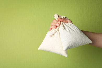 Photo of Woman holding full cotton eco bags on light green background, closeup. Space for text