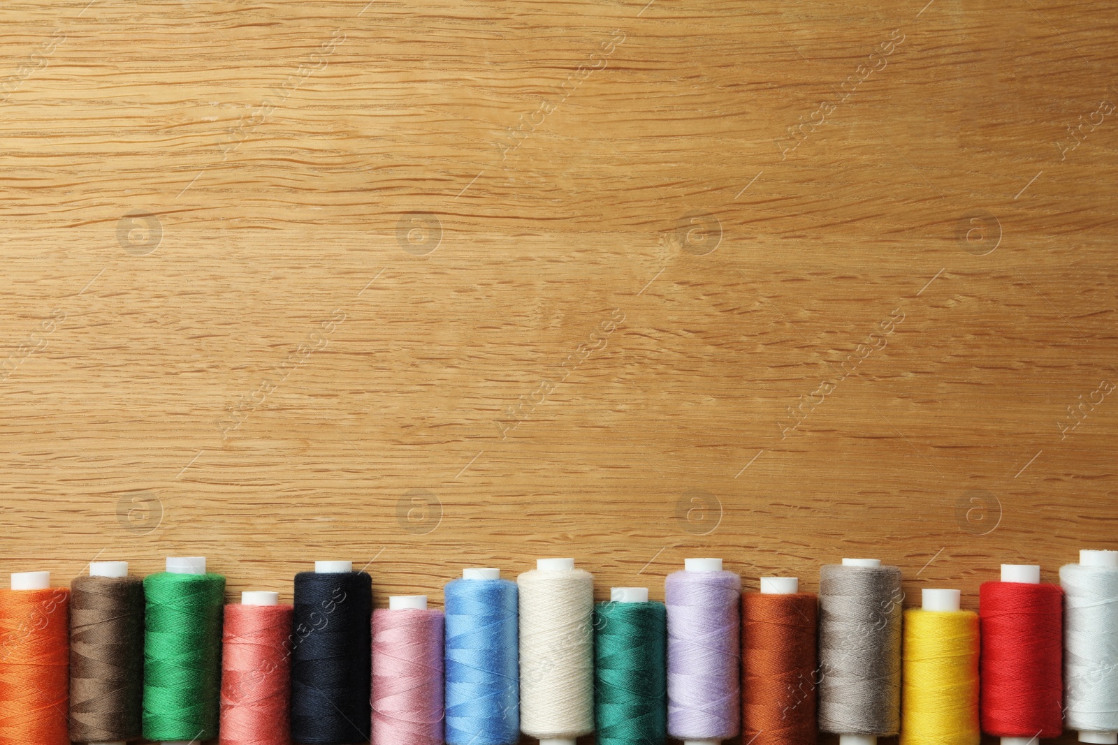 Photo of Many colorful sewing threads on wooden table, flat lay. Space for text