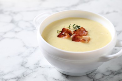 Tasty potato soup with bacon and rosemary in bowl on white marble table, closeup. Space for text