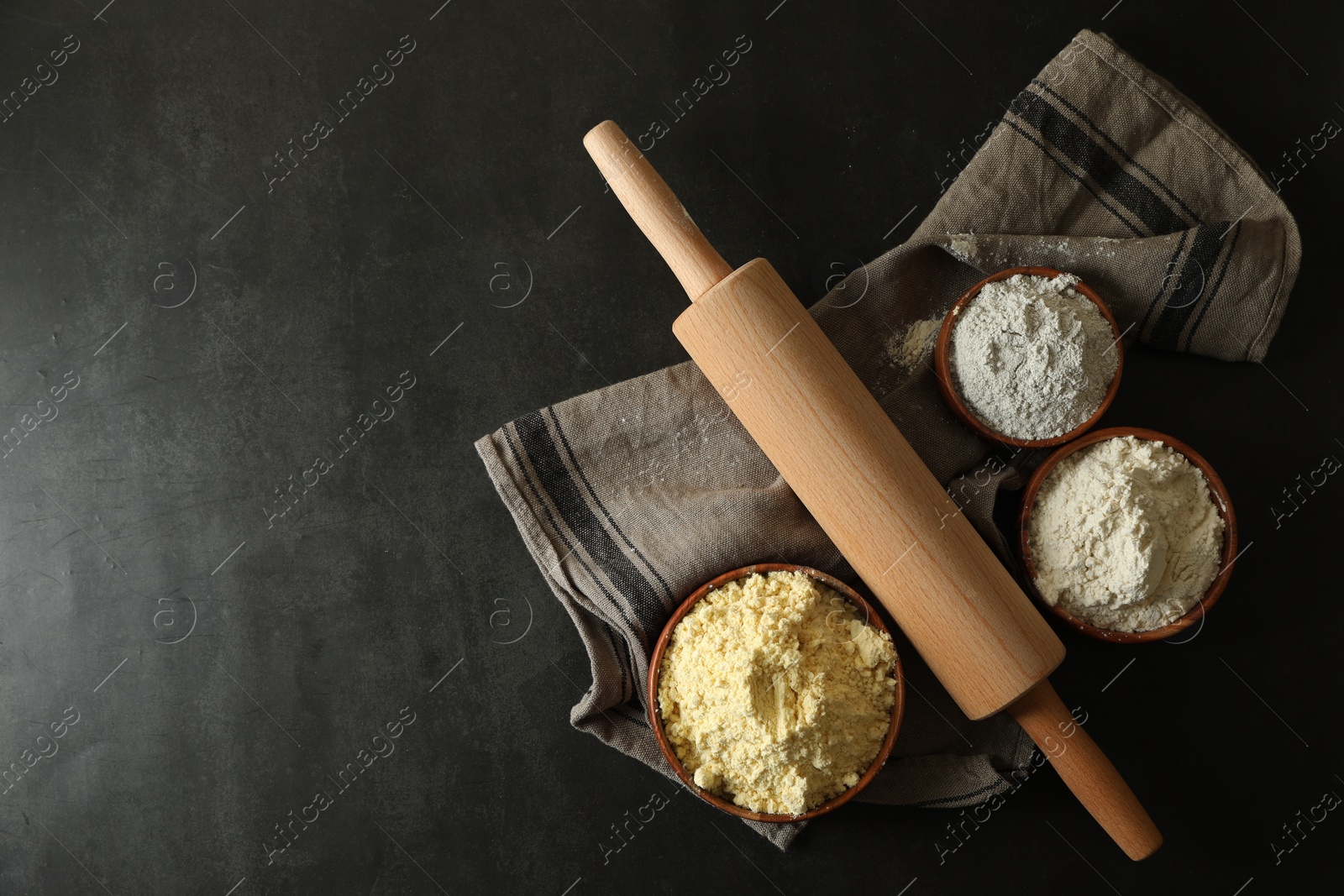 Photo of Rolling pin and different types of flour on black table, top view. Space for text