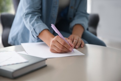 Photo of Woman writing letter at table indoors, closeup