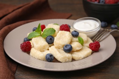 Photo of Plate of tasty lazy dumplings with berries, sour cream and mint leaves on wooden table