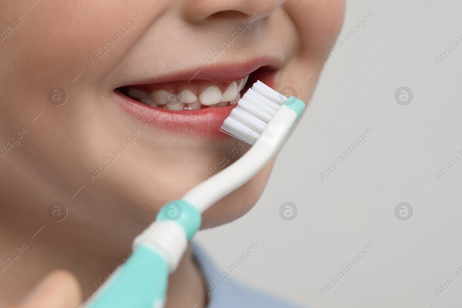 Photo of Cute little boy brushing his teeth with plastic toothbrush on light grey background, closeup. Space for text