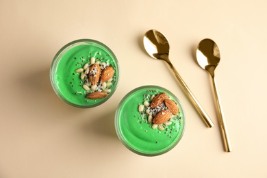 Glass cups of spirulina smoothie and spoons on color background, flat lay