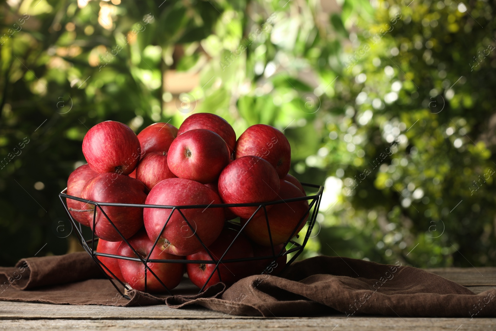 Photo of Ripe red apples in bowl on wooden table outdoors, space for text