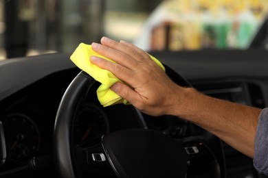 Man cleaning steering wheel with rag in car, closeup