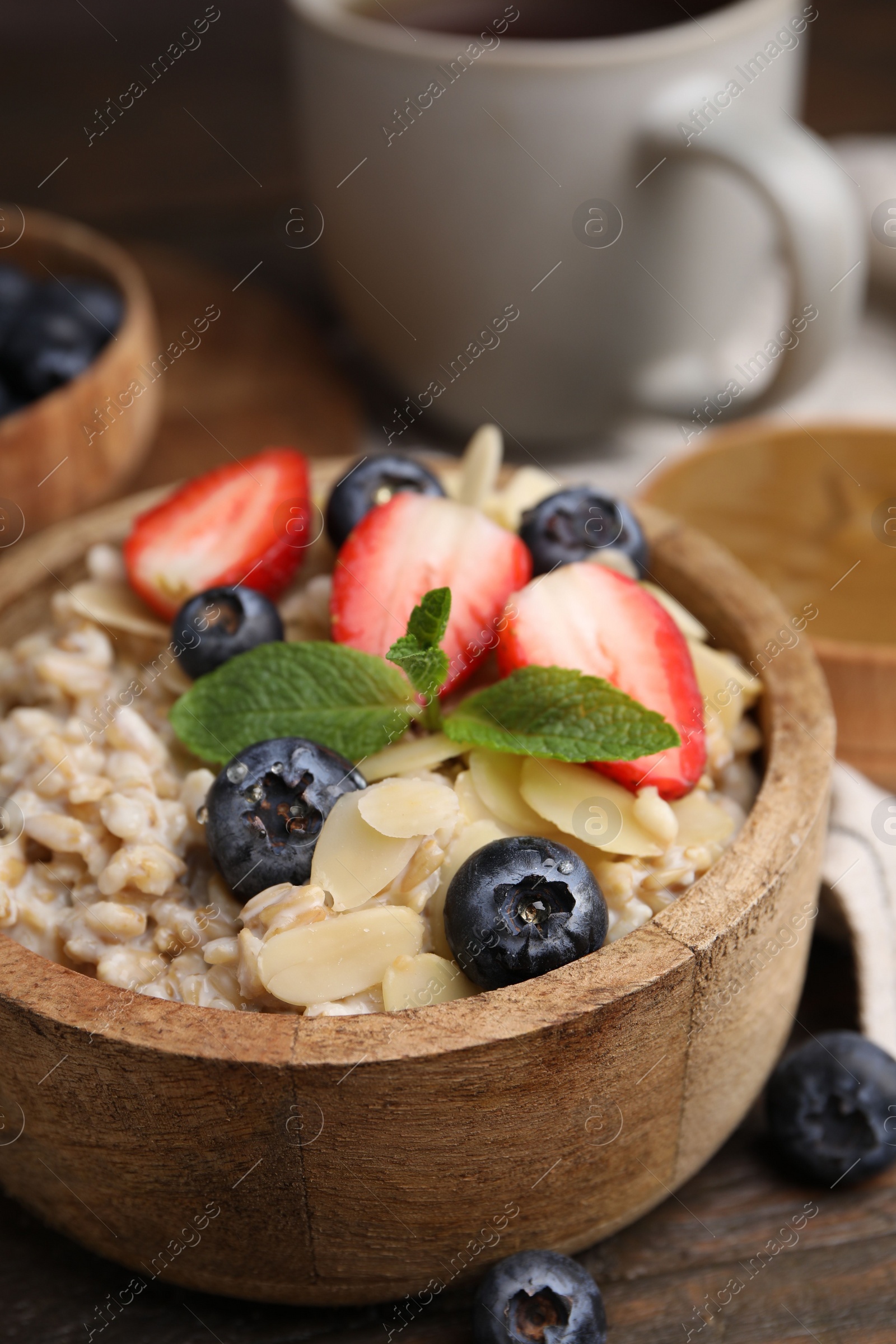 Photo of Tasty oatmeal with strawberries, blueberries and almond flakes in bowl on wooden table, closeup