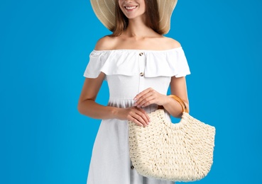 Young woman with stylish straw bag on light blue background, closeup