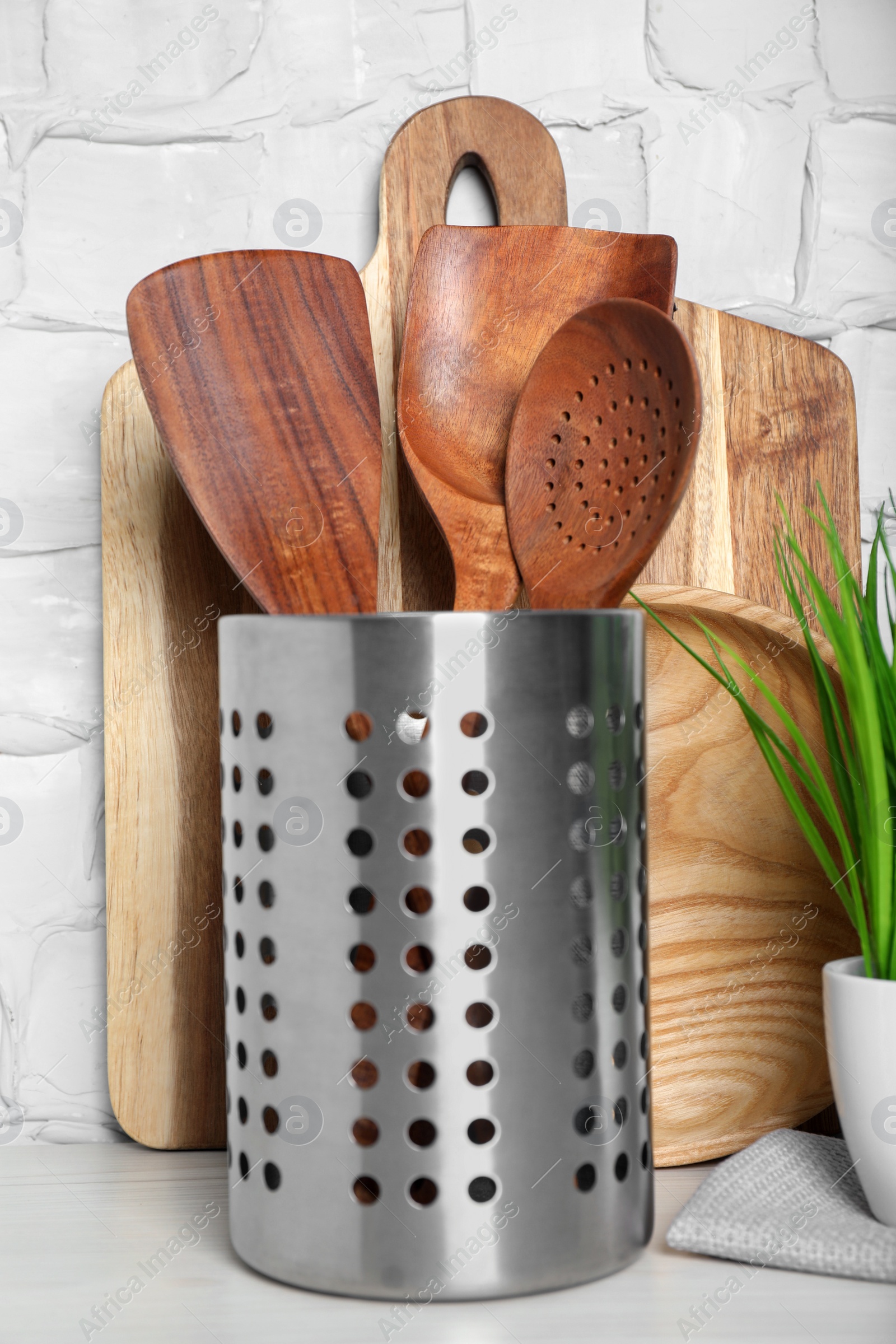 Photo of Set of wooden kitchen utensils, board and houseplant on table near white wall