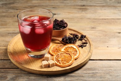 Photo of Delicious iced hibiscus tea, dried orange slices, flowers and brown sugar on wooden table, space for text