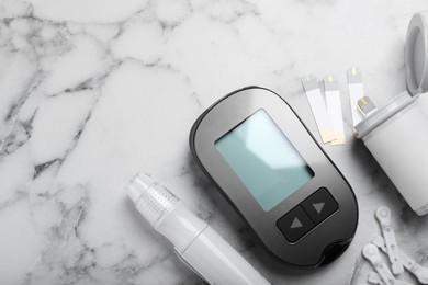 Photo of Glucometer, lancet pen and strips on white marble table, flat lay with space for text. Diabetes testing kit