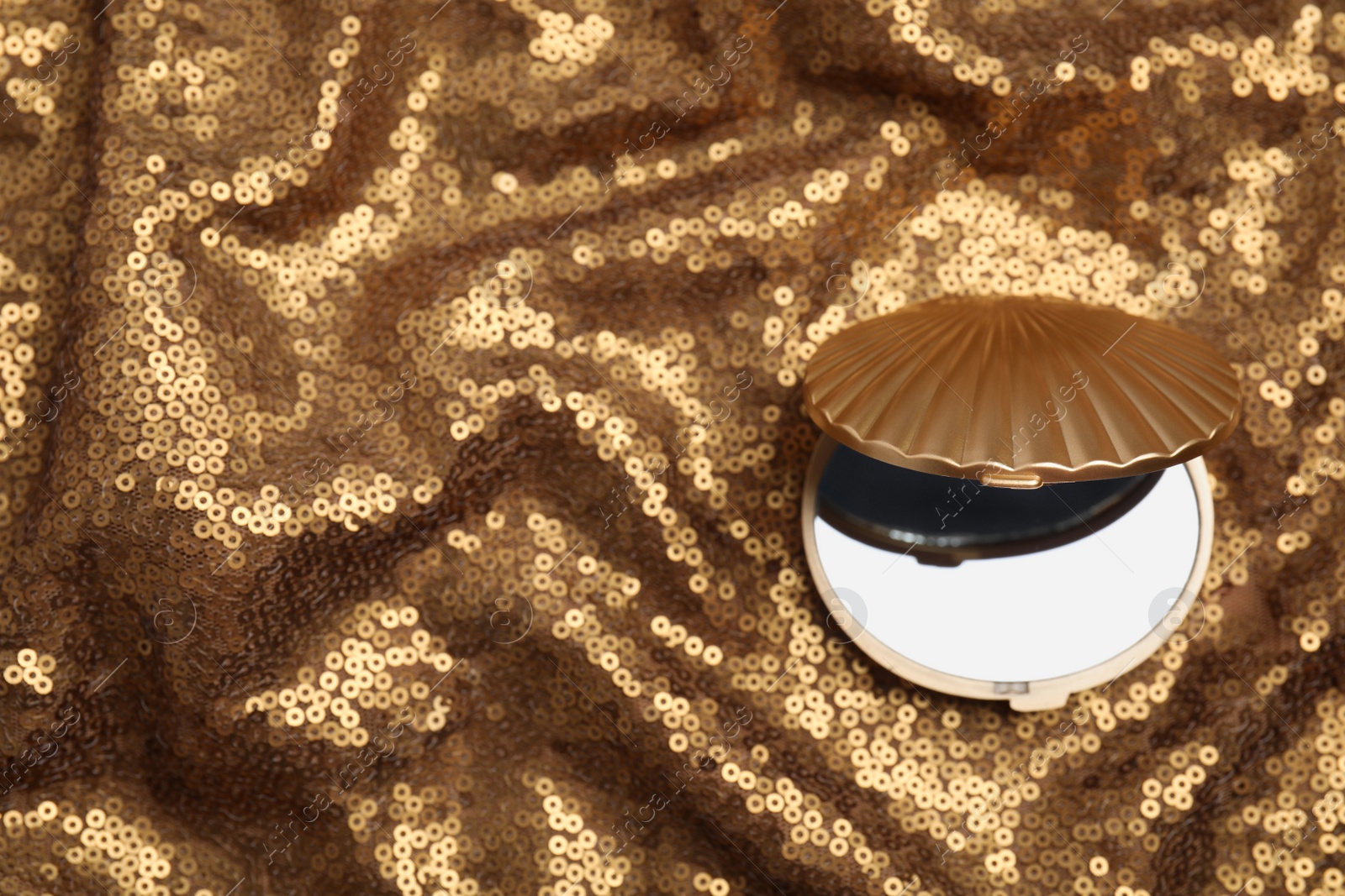 Photo of Bright cosmetic pocket mirror on gold fabric, top view. Space for text