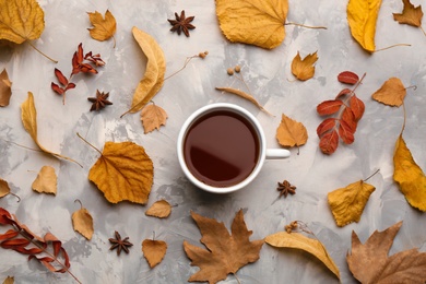 Photo of Cup of hot drink and autumn leaves on grey table, flat lay. Cozy atmosphere