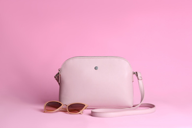 Stylish woman's bag and sunglasses on light pink background