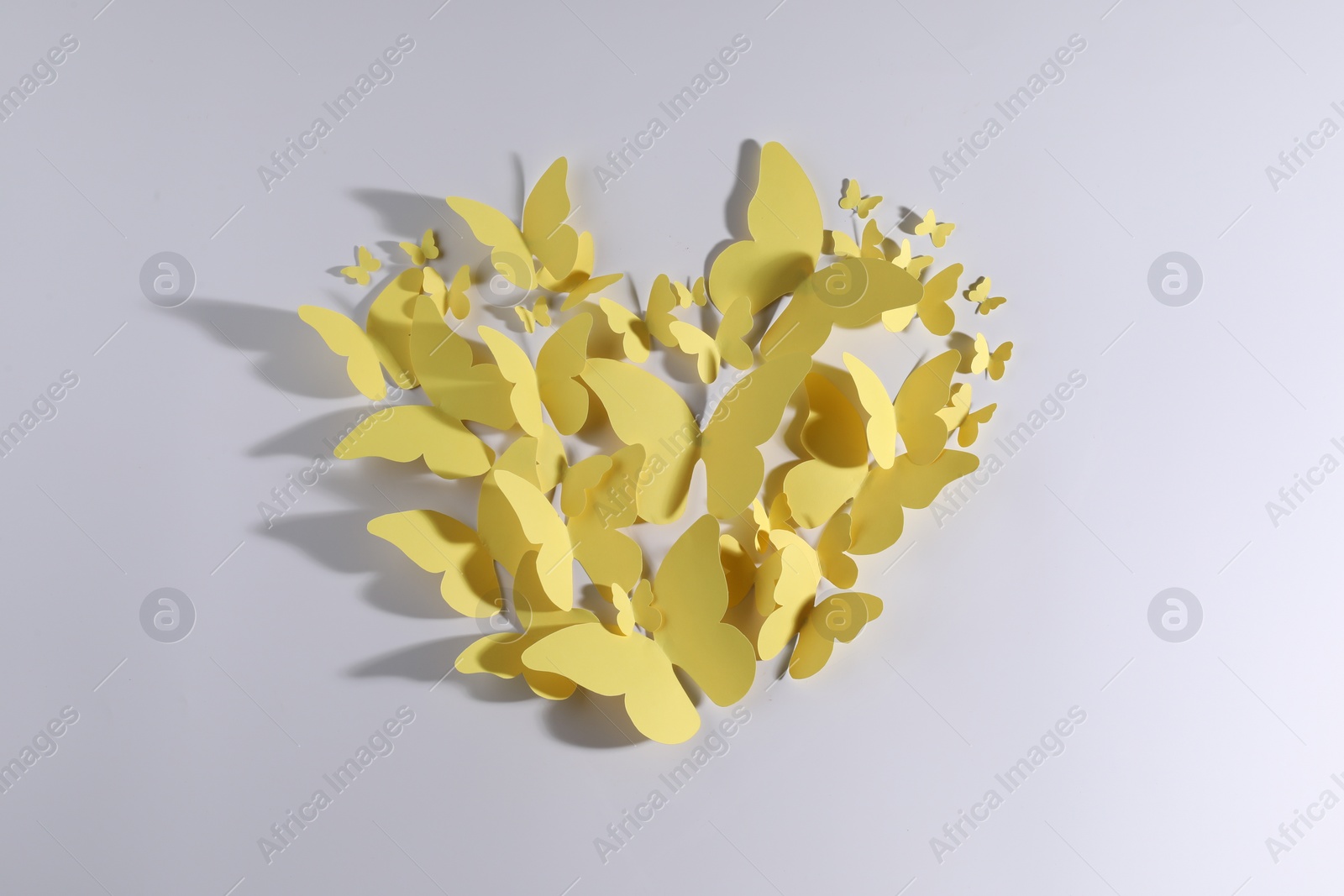 Photo of Heart shape made of yellow paper butterflies on white background, top view