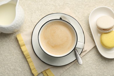 Tasty cappuccino in cup, milk and macarons on light textured table, flat lay