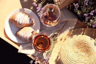 Plate with croissants and glasses of wine on wooden tray in lavender field, top view