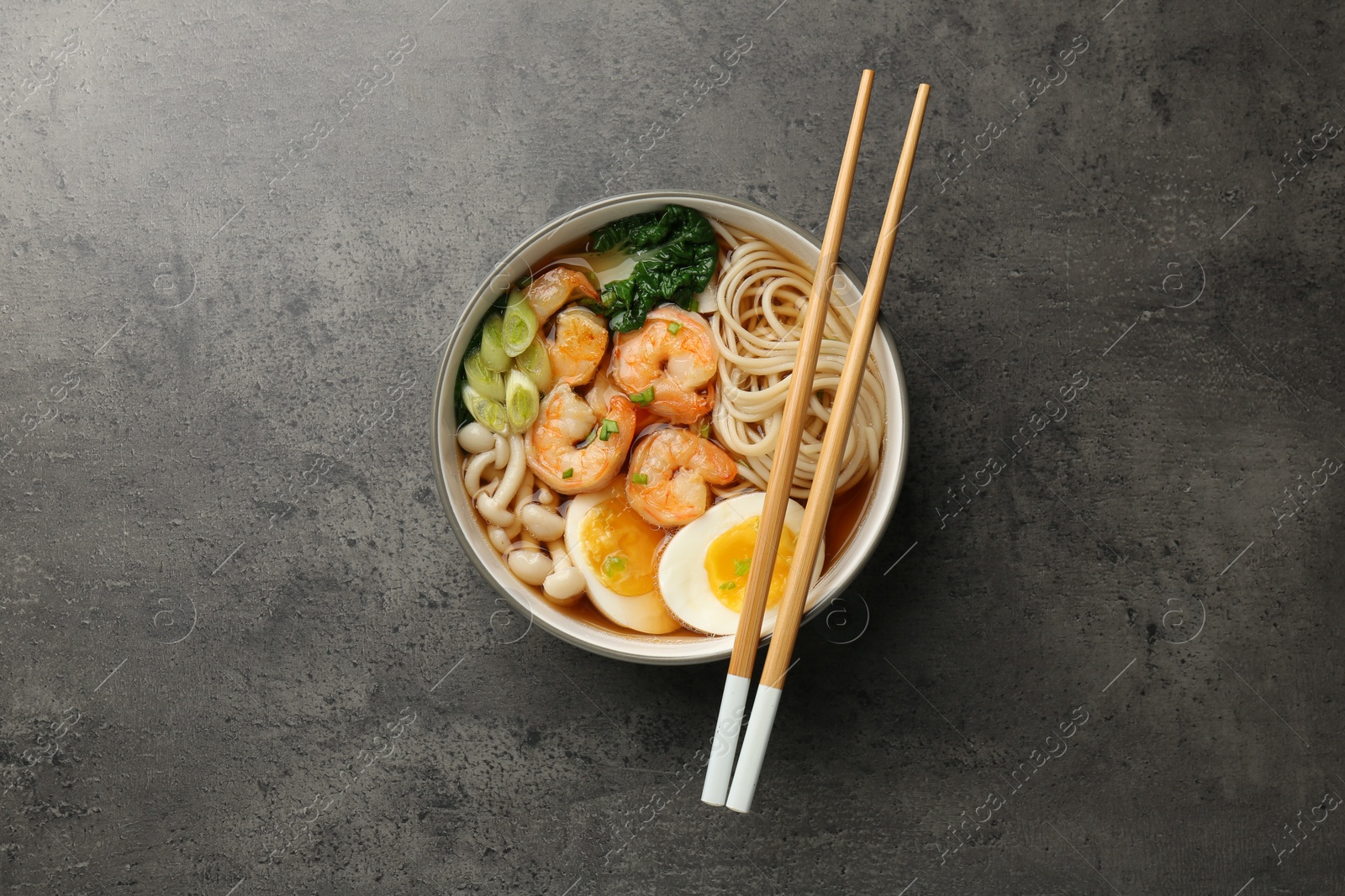 Photo of Delicious ramen with shrimps and chopsticks on grey table, top view. Noodle soup